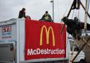 Animal Rebellion protesters suspended from a bamboo structure and on top of a van, being monitored by police officers, outside a McDonalds distribution site in Basingstoke,