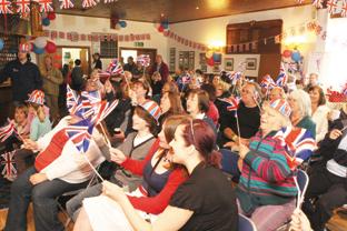 People wave their flags as Kate while watching the wedding on the tv in Upton