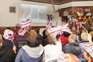 People wave their flags as Kate while watching the wedding on the tv in Upton 
