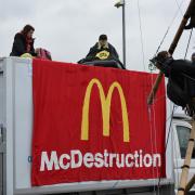 Animal Rebellion protesters suspended from a bamboo structure and on top of a van, being monitored by police officers, outside a McDonalds distribution site in Basingstoke,